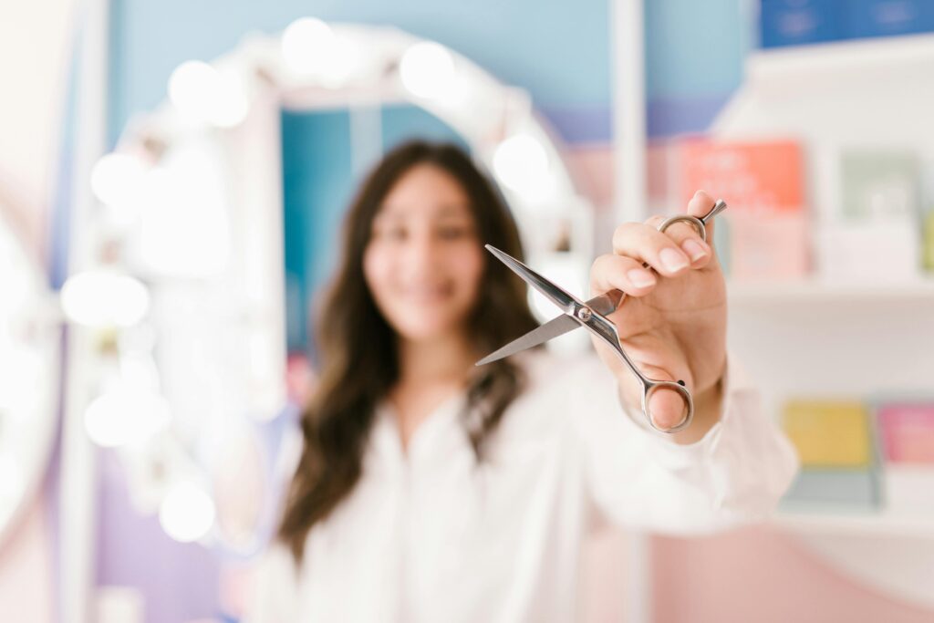 Hairdresser showcasing scissors in a bright, modern salon with blurred background for professional service.